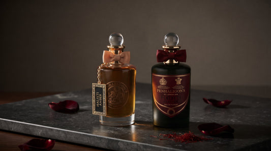 Penhaligon's Halfeti Amber and Halfeti Leather bottles on dark honed stone with dark crimson rose petals and saffron threads