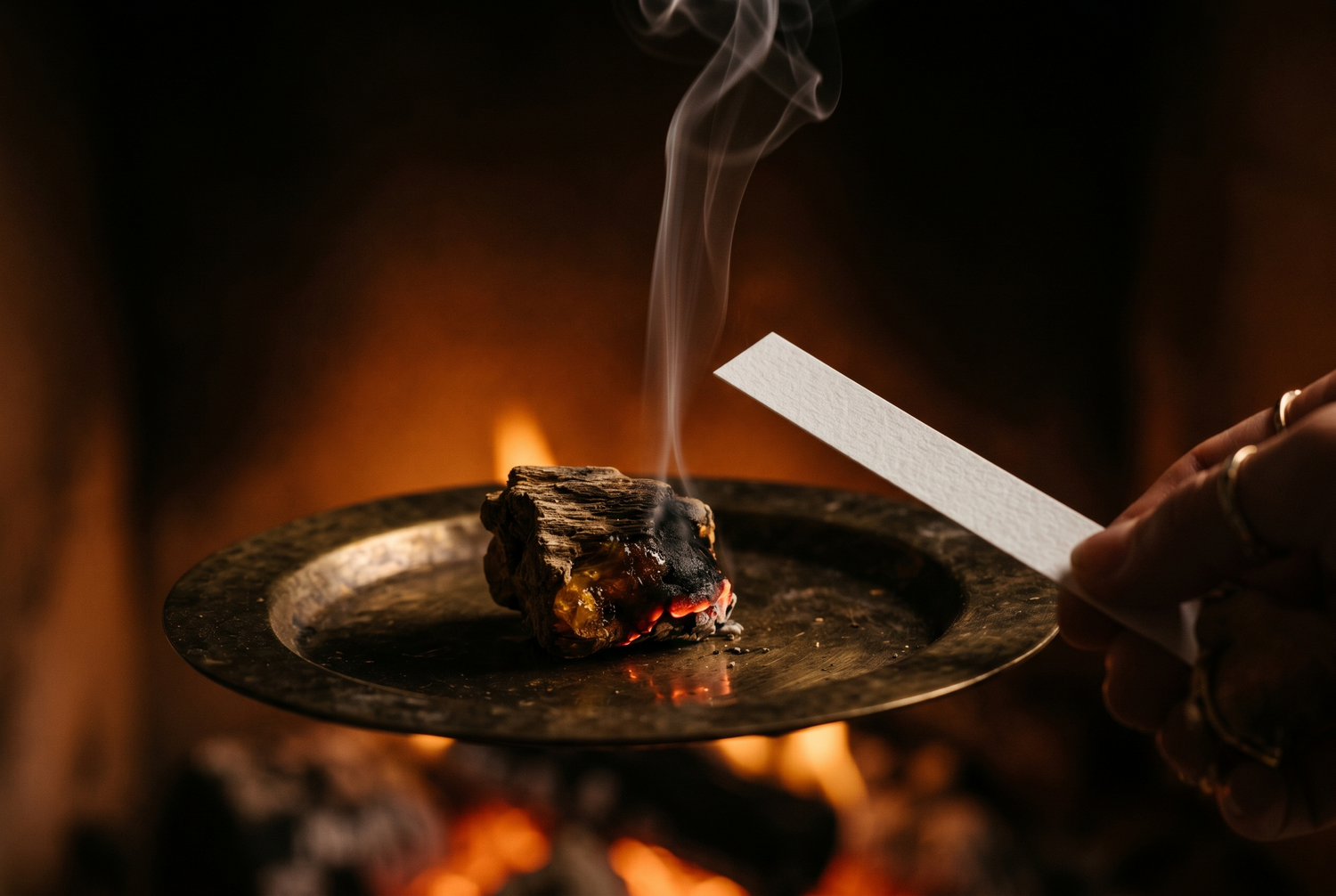 Fragrant smoke rising from burning agarwood on a brass incense plate with a white paper test strip, the direct sensory signature of real oud