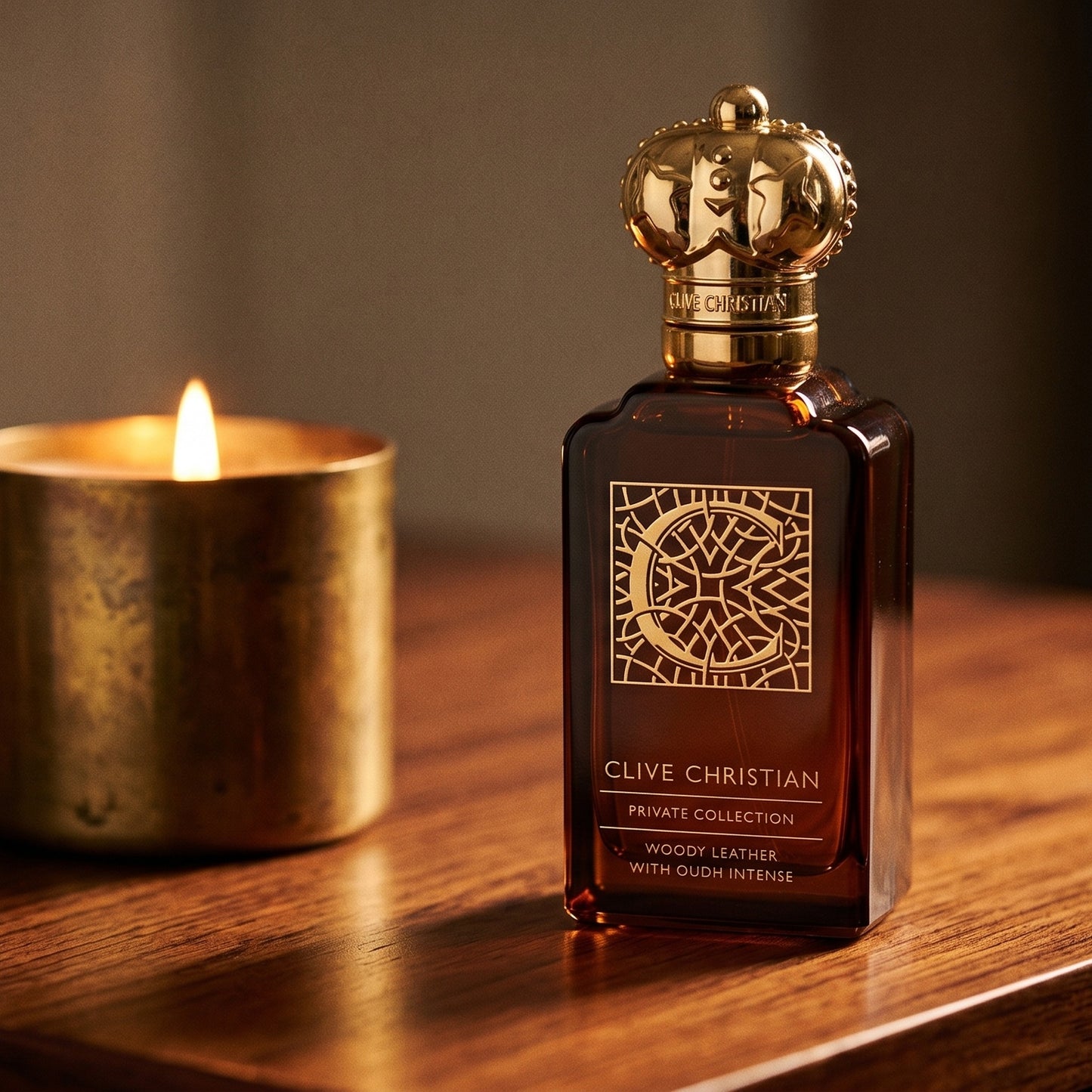 Clive Christian Private Collection (Woody/Leather/Oud/Amber) on rosewood surface with a squat brass candle flickering nearby