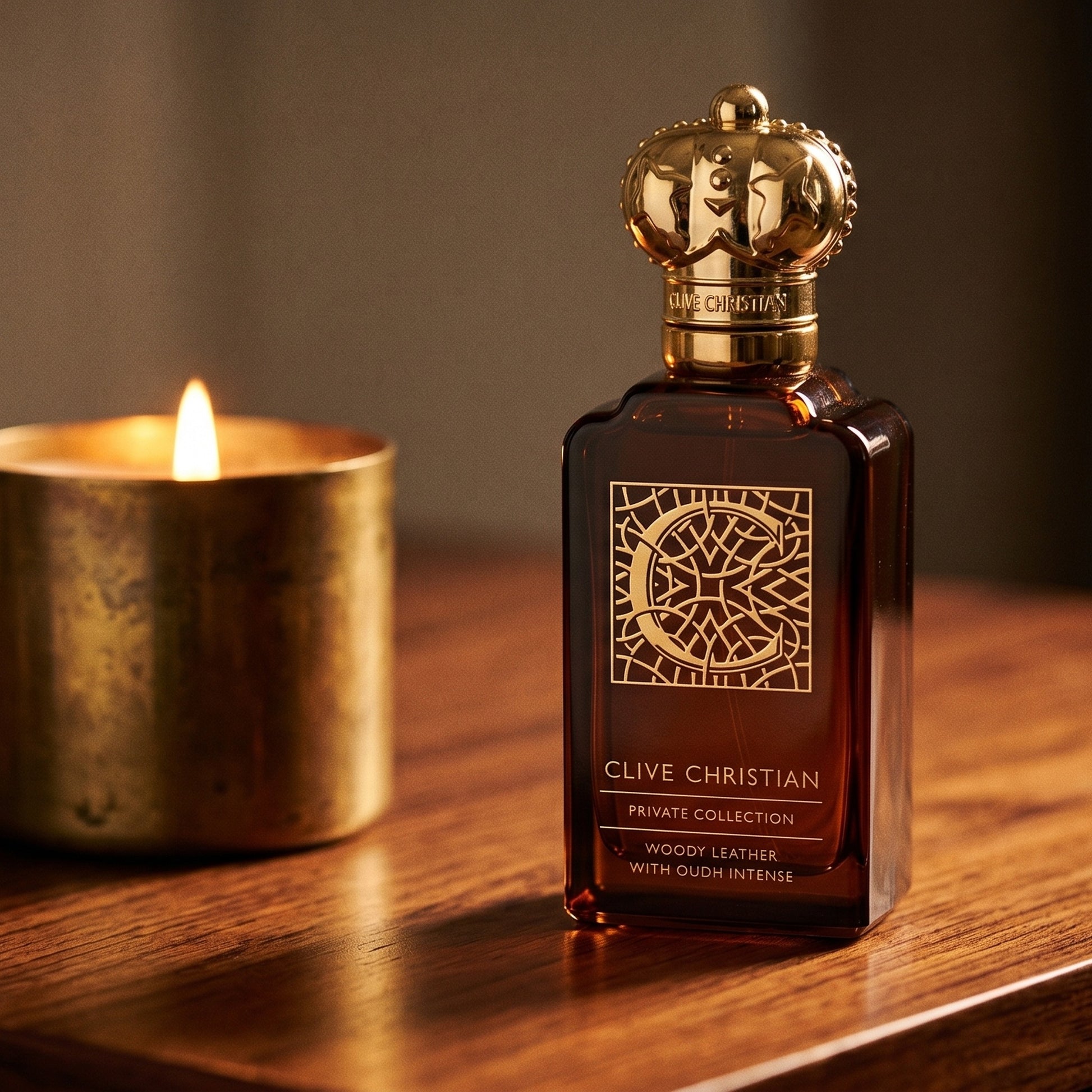 Clive Christian Private Collection (Woody/Leather/Oud/Amber) on rosewood surface with a squat brass candle flickering nearby