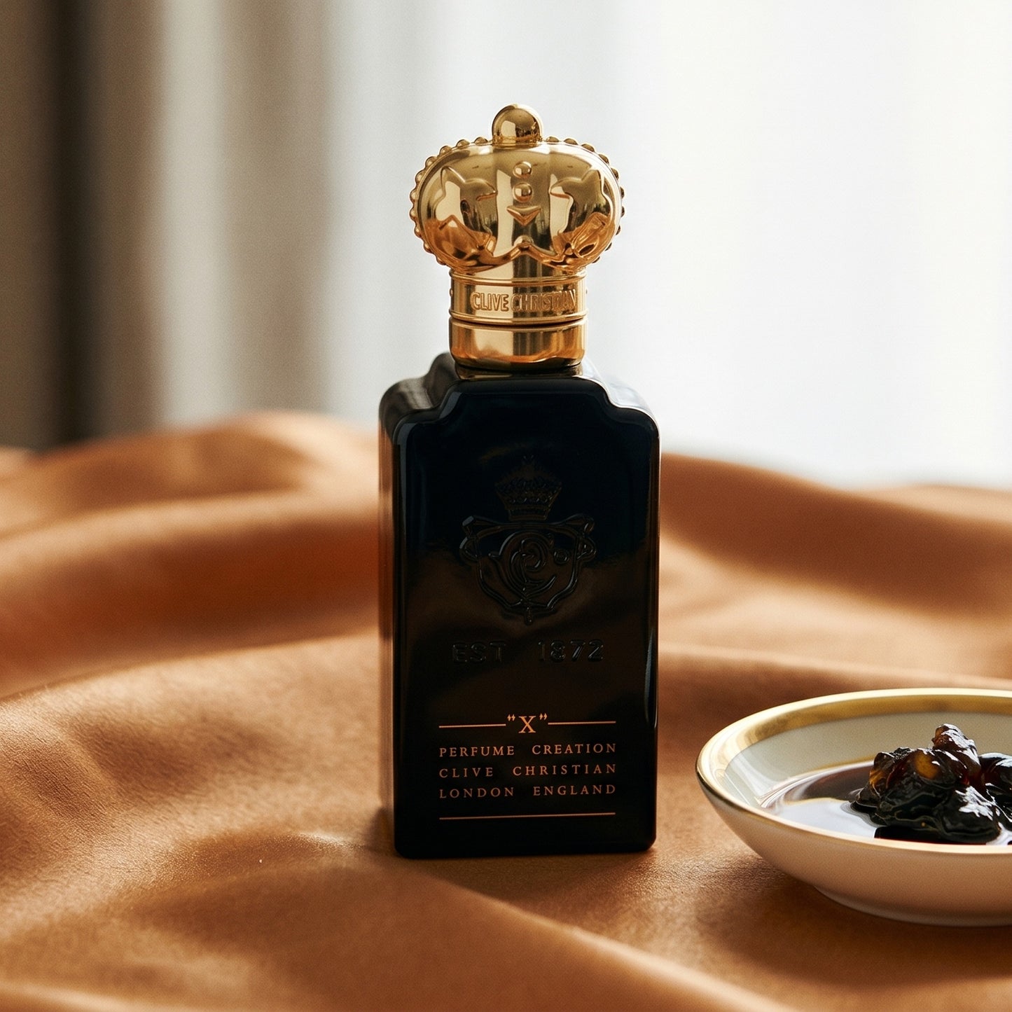 Clive Christian X on amber-toned satin with a gold-rim ceramic dish of labdanum