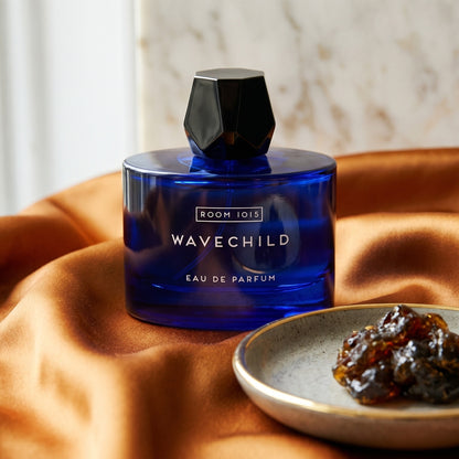 Room 1015 Wavechild EDP on amber-toned satin with a gold-rim ceramic dish of labdanum