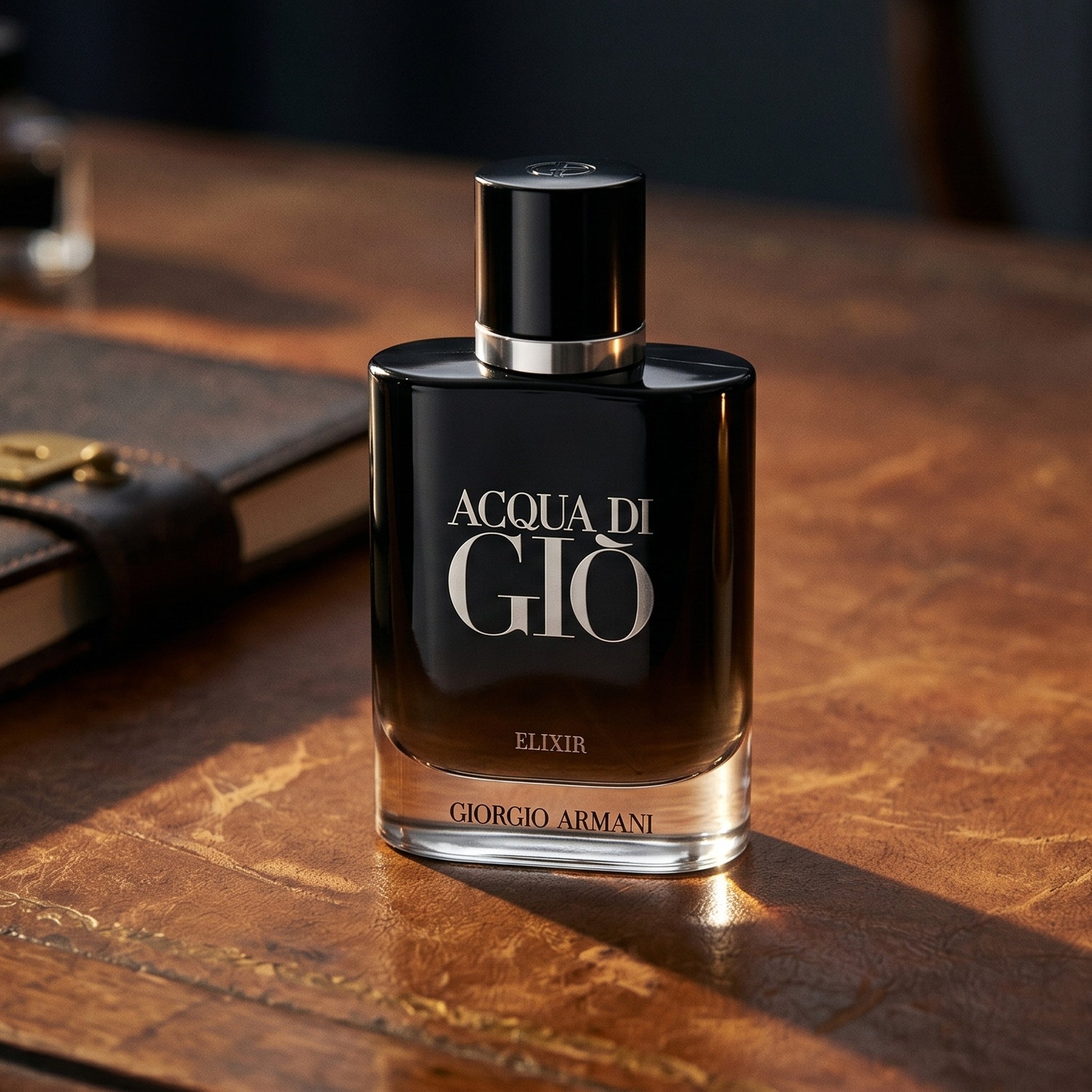 Acqua di Gio Elixir on worn tobacco leather desk with a leather-bound notebook nearby