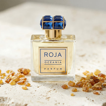 Roja Oceania Parfum on cream stone with a scatter of honey-colored ambergris flakes