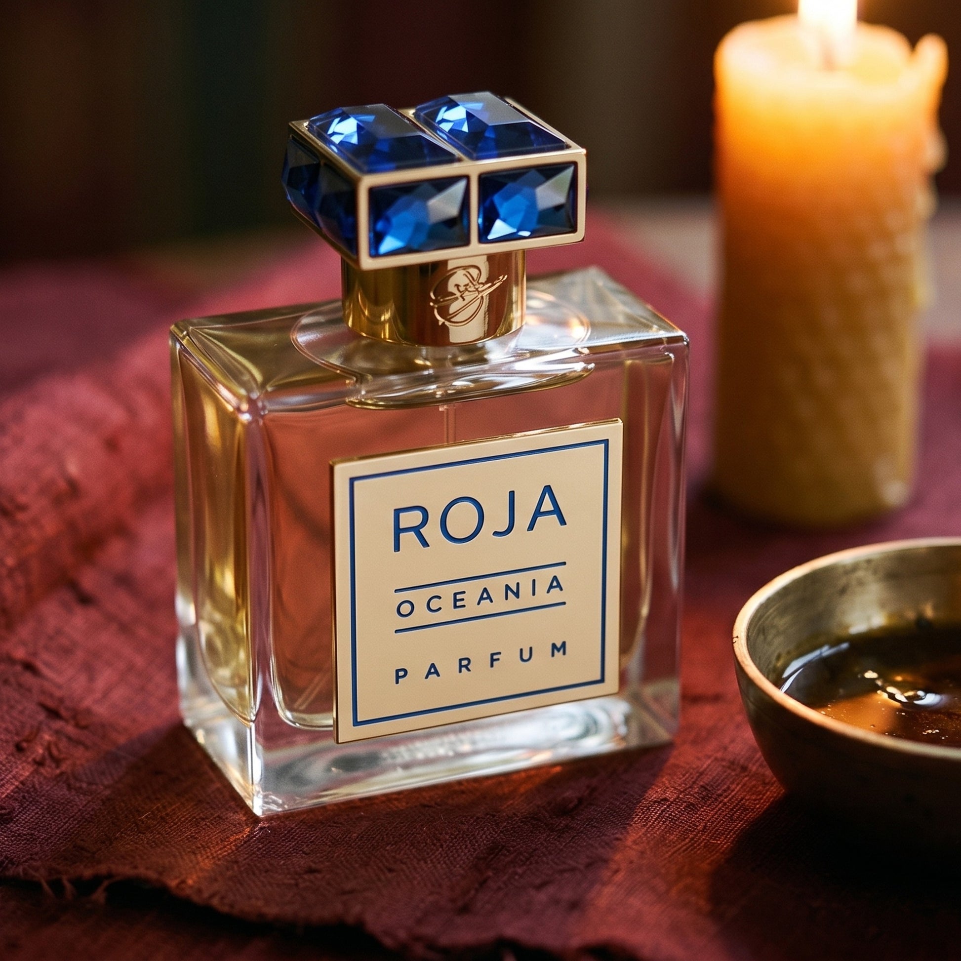 Roja Oceania Parfum on raw silk of oxblood color with a brass bowl of ambergris tincture