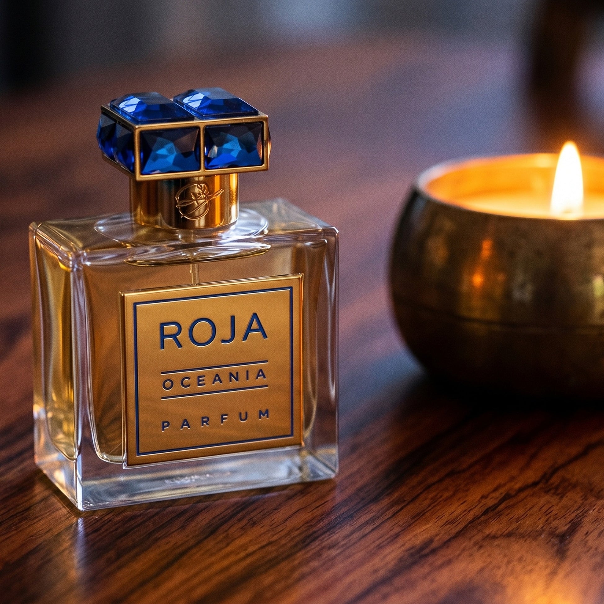 Roja Oceania Parfum on rosewood surface with a squat brass candle flickering nearby