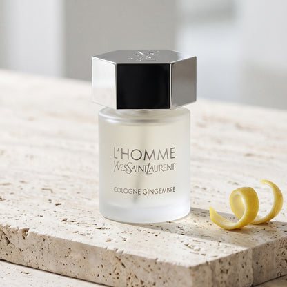 Yves Saint Laurent Lhomme Gingembre Cologne on pale travertine with a lemon peel curled beside the bottle
