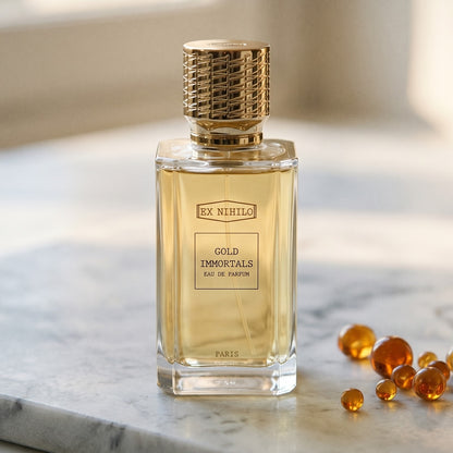 Ex Nihilo Gold Immortals EDP on pale grey marble with amber resin beads scattered to one side