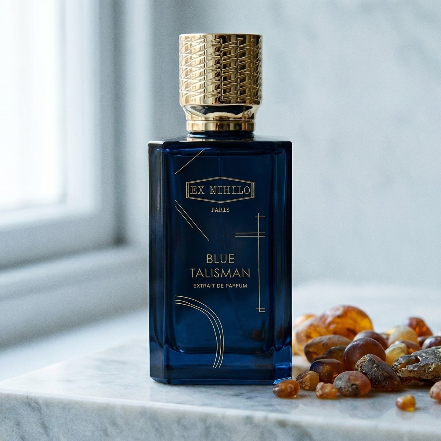 Ex Nihilo Gold Immortals Extrait EDP on pale grey marble with amber resin beads scattered to one side