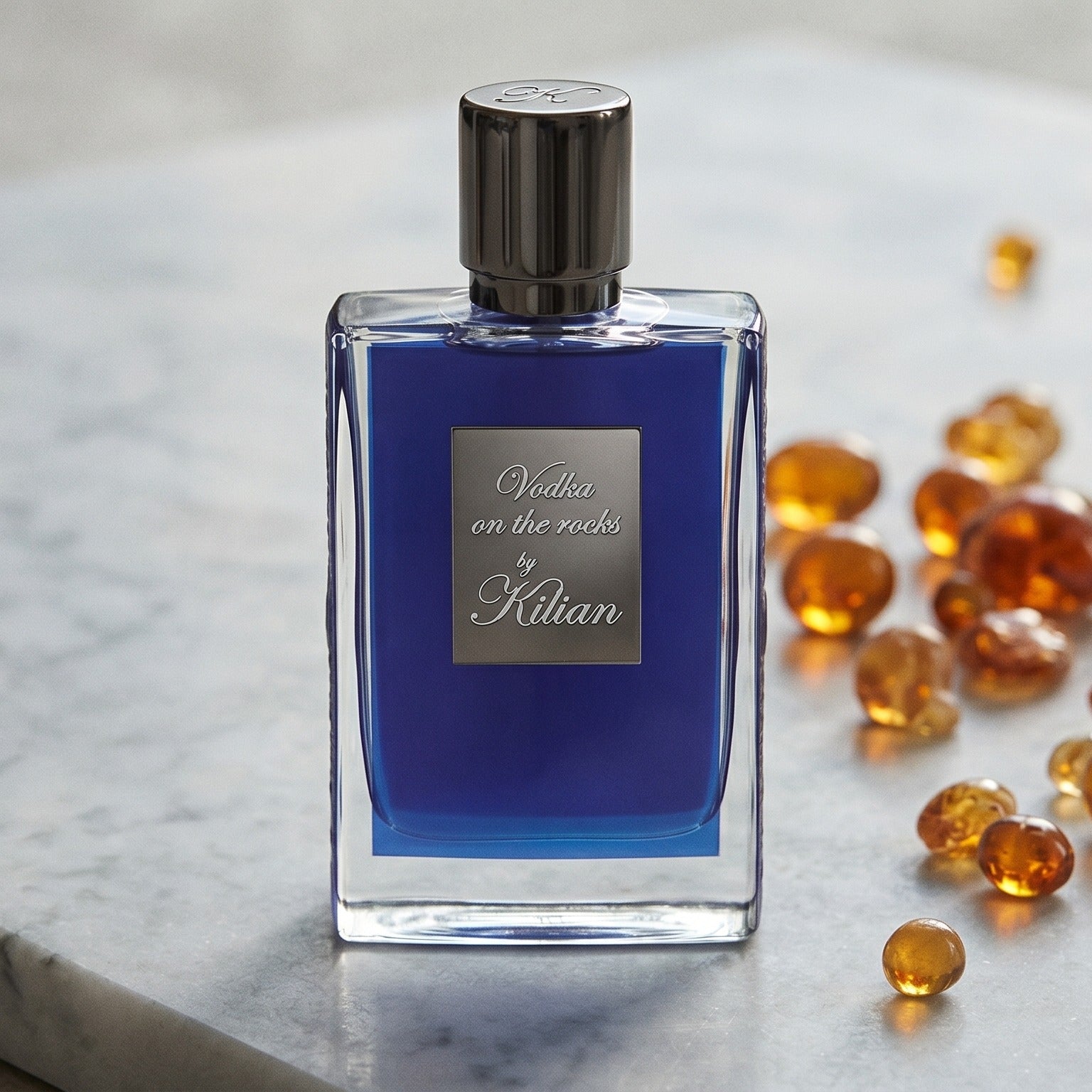 Kilian Vodka On The Rocks EDP on pale grey marble with amber resin beads scattered to one side