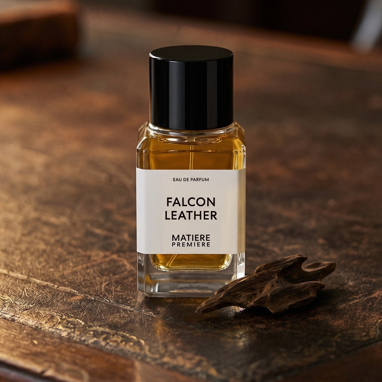 Matiere Premiere Falcon Leather EDP on aged leather-topped desk with a single agarwood chip beside the bottle