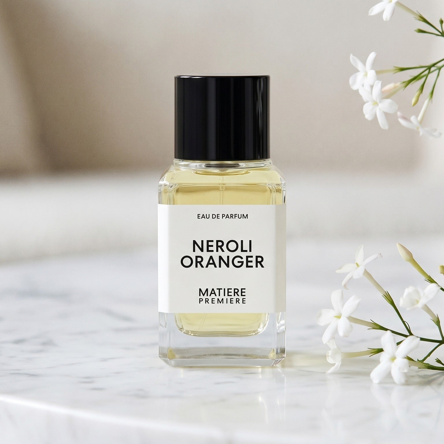 Matiere Premiere Neroli Oranger EDP on white carrara marble with jasmine sprigs placed to frame-right