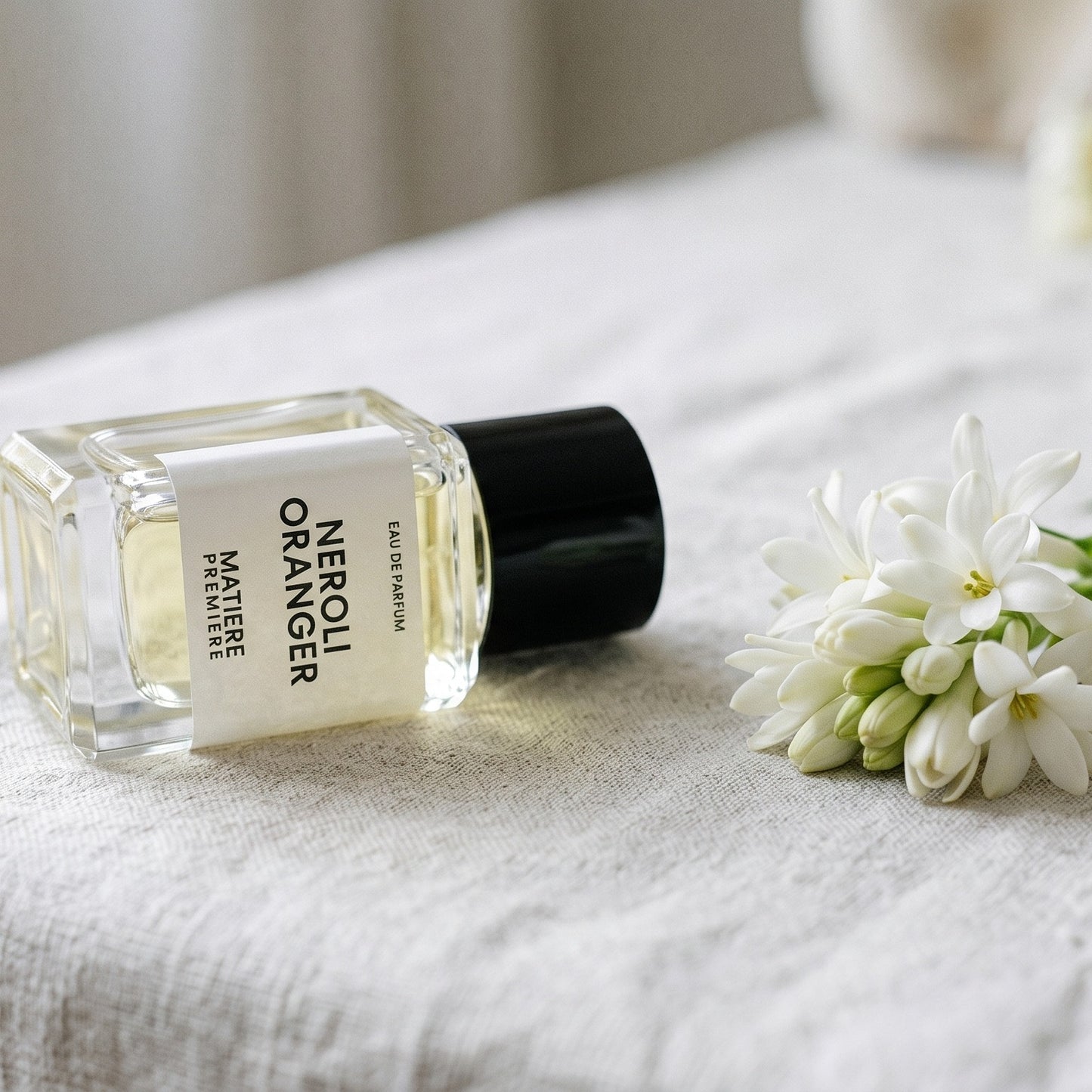 Matiere Premiere Neroli Oranger EDP on bleached linen with a single tuberose stem laid flat
