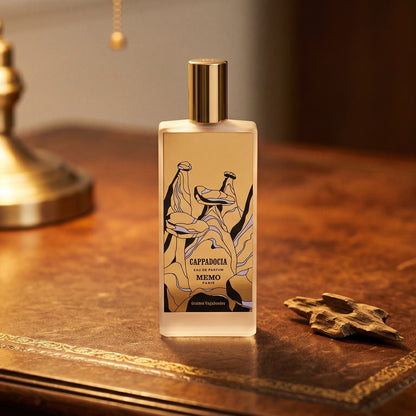 Memo Paris Cappadocia EDP on aged leather-topped desk with a single agarwood chip beside the bottle