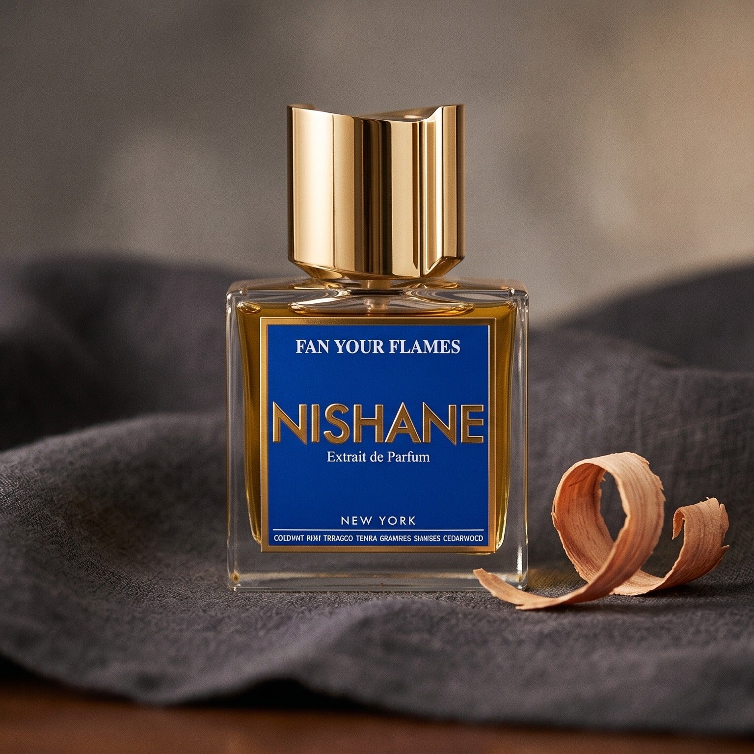 Nishane Fan Your Flames on charcoal linen with a curl of cedarwood shaving beside the bottle