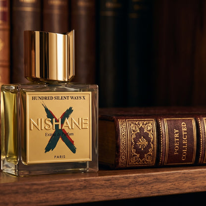 Nishane Hundred Silent Ways X Extrait on dark walnut library shelf with a leather-bound book with gold foil