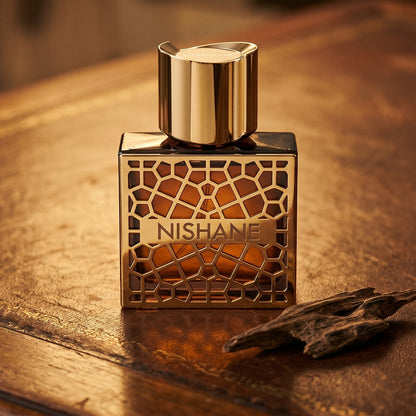 Nishane Nefs EDP on aged leather-topped desk with a single agarwood chip beside the bottle
