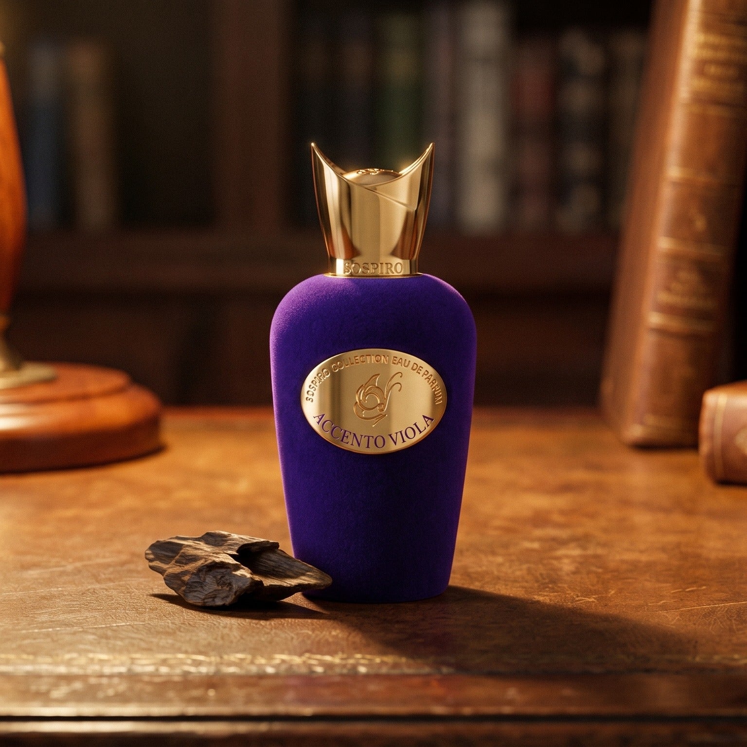 Sospiro Accento Viola EDP on aged leather-topped desk with a single agarwood chip beside the bottle