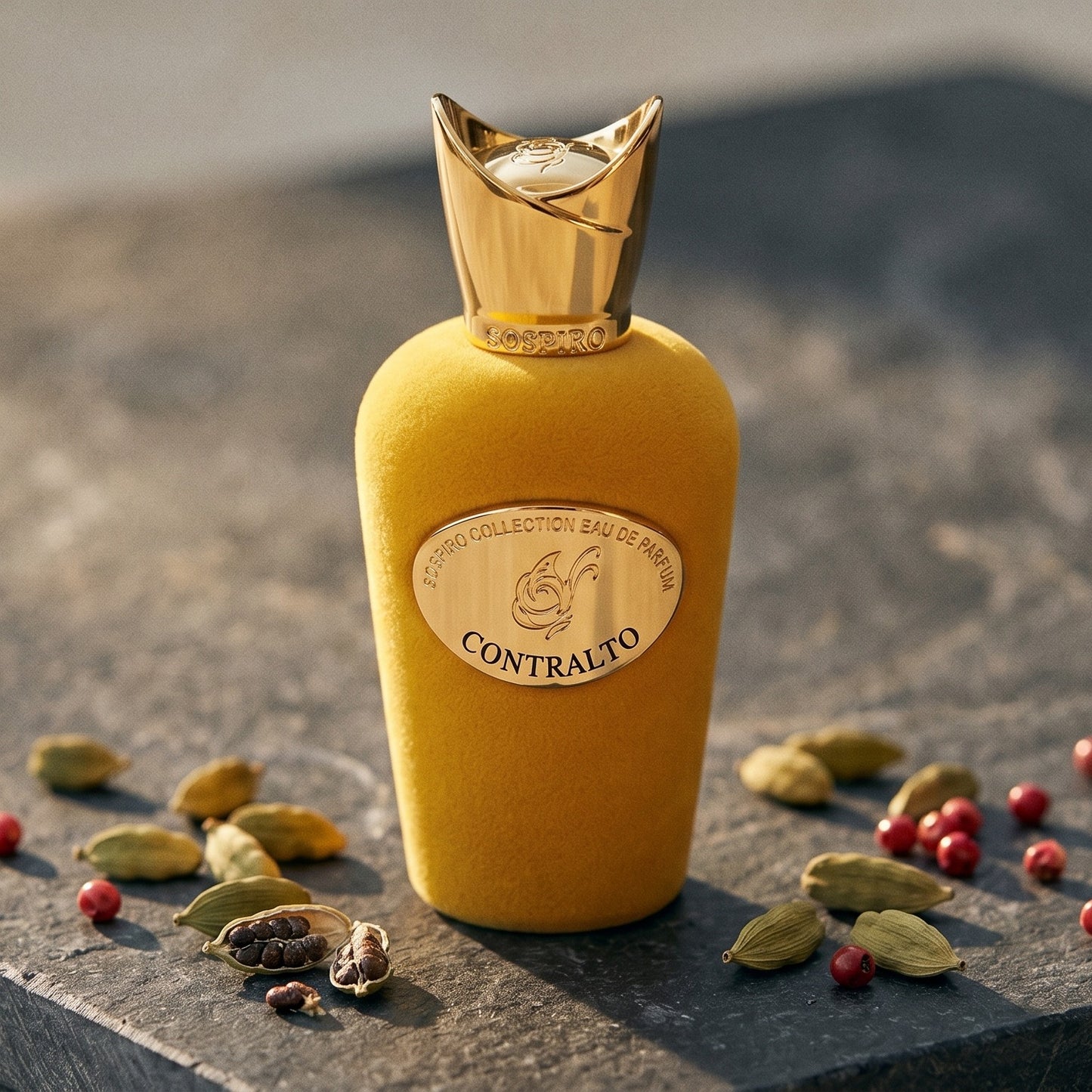 Sospiro Contralto EDP on dark grey stone slab with cardamom pods and pink peppercorns scattered