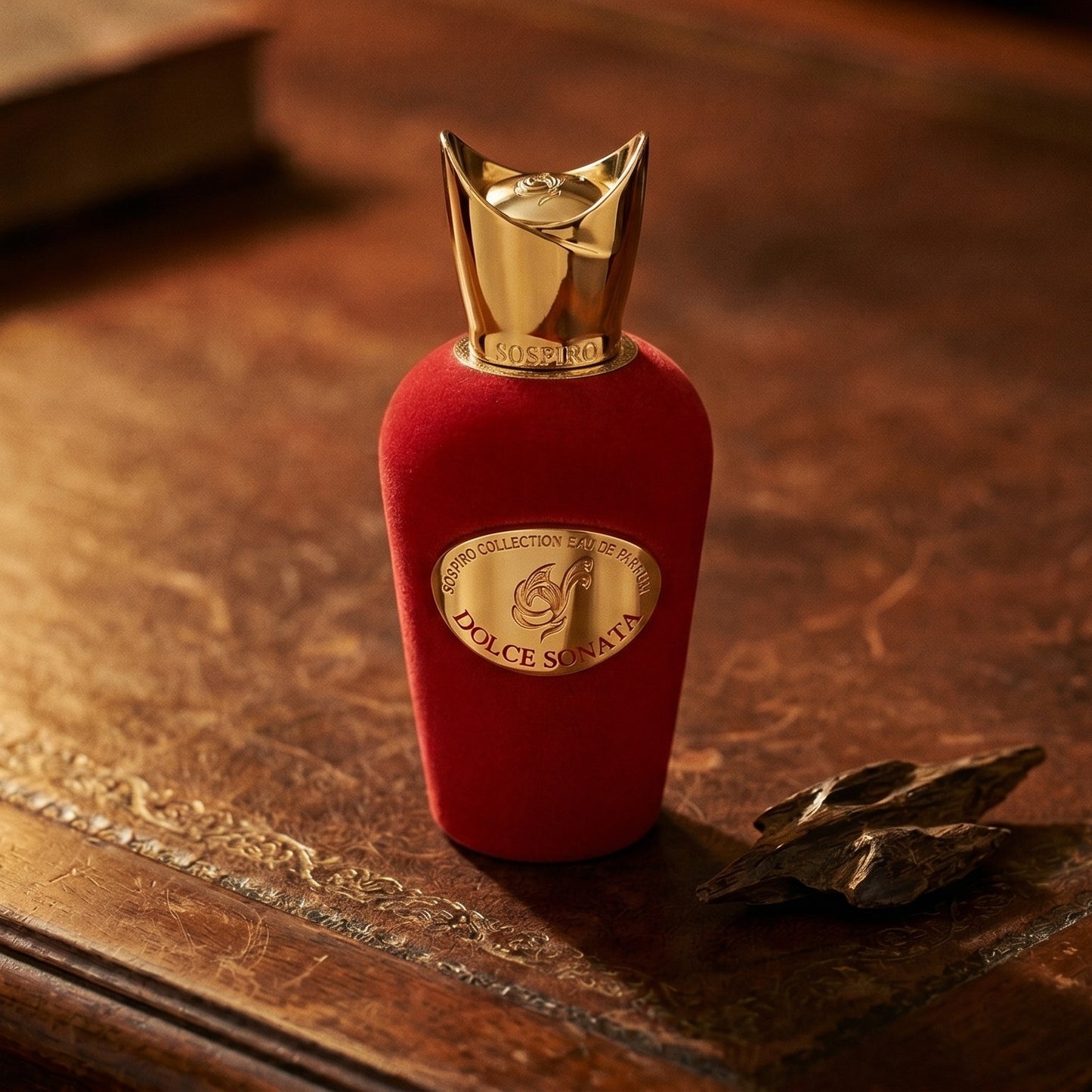 Sospiro Dolce Sonata EDP on aged leather-topped desk with a single agarwood chip beside the bottle