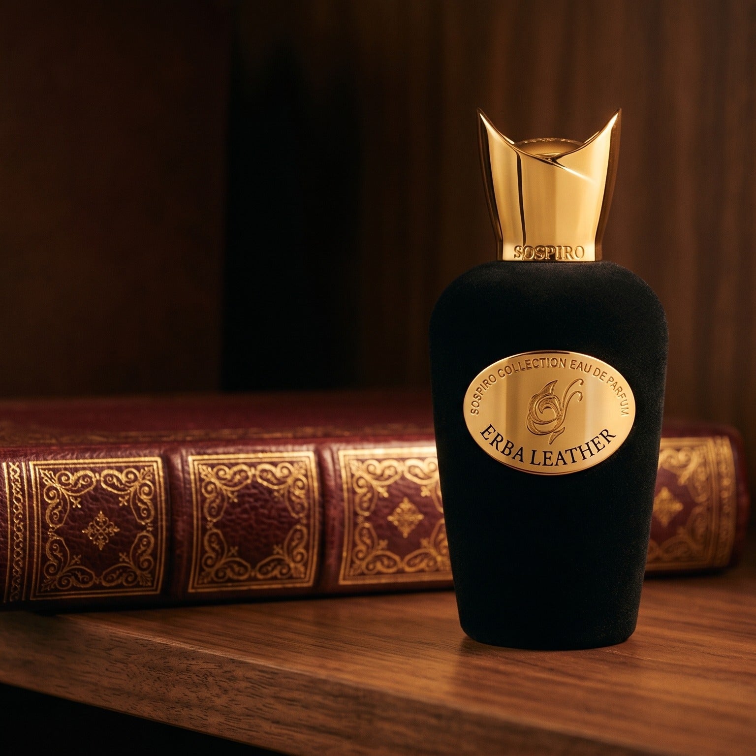 Sospiro Erba Leather EDP on dark walnut library shelf with a leather-bound book with gold foil