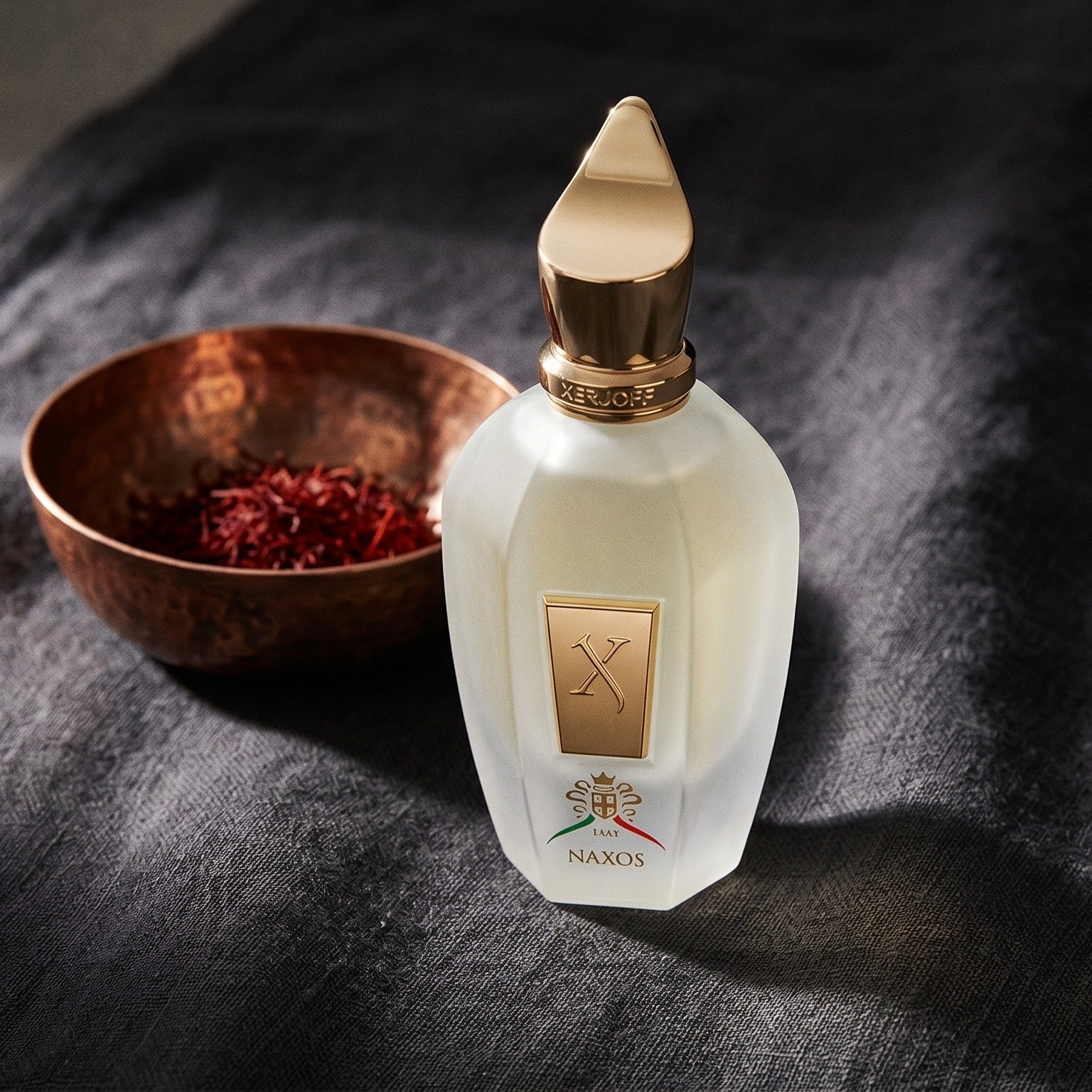 Xerjoff Naxos EDP on charcoal linen with a small copper bowl of saffron threads