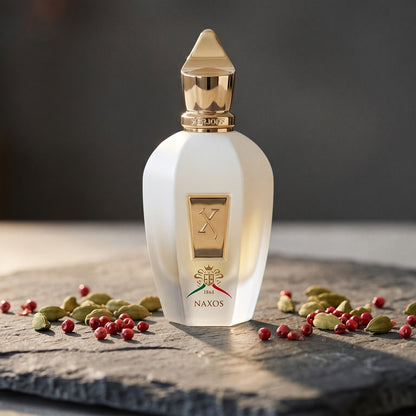 Xerjoff Naxos EDP on dark grey stone slab with cardamom pods and pink peppercorns scattered