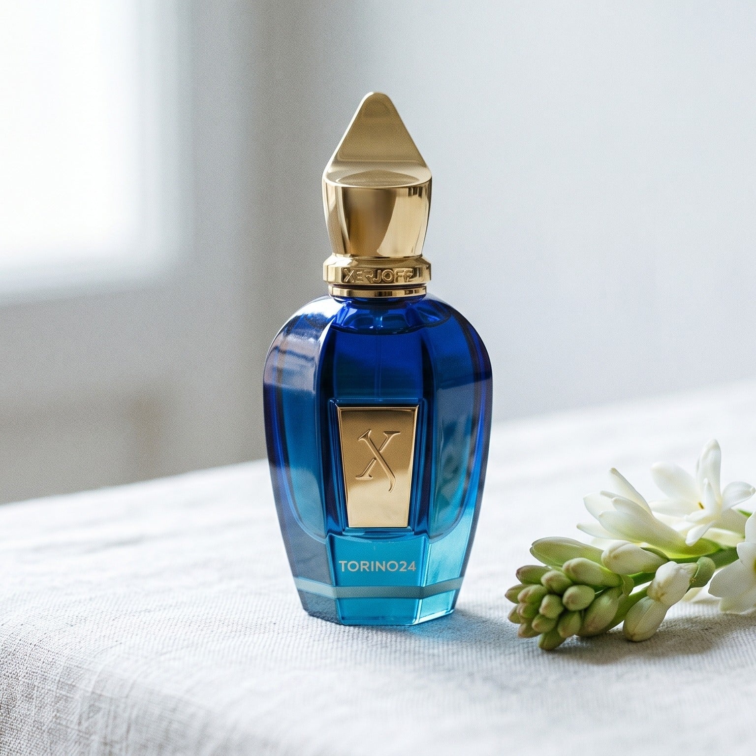 Xerjoff Torino 24 EDP on bleached linen with a single tuberose stem laid flat