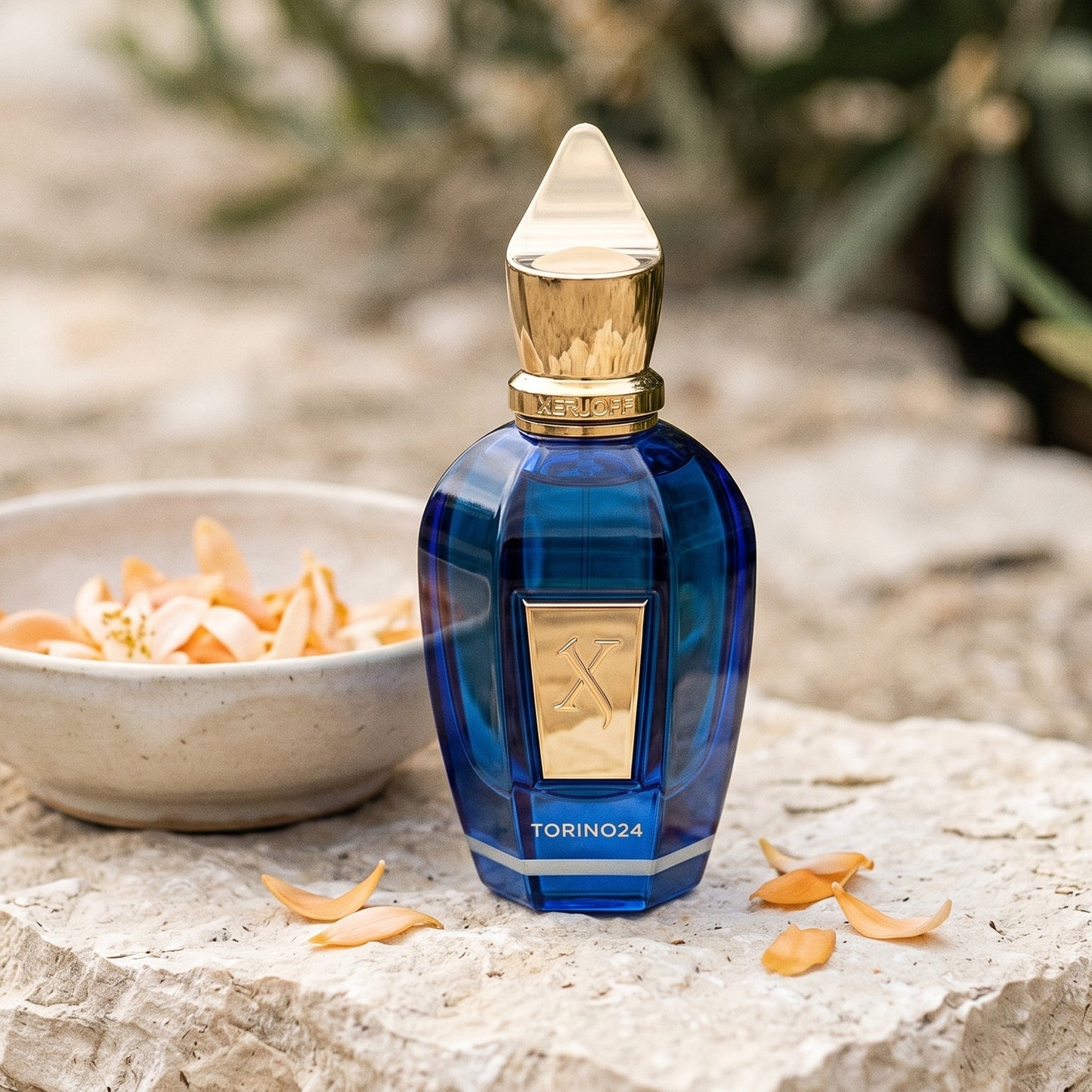 Xerjoff Torino 24 EDP on pale stone with orange-blossom petals in a shallow bowl