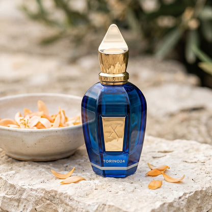 Xerjoff Torino 24 EDP on pale stone with orange-blossom petals in a shallow bowl