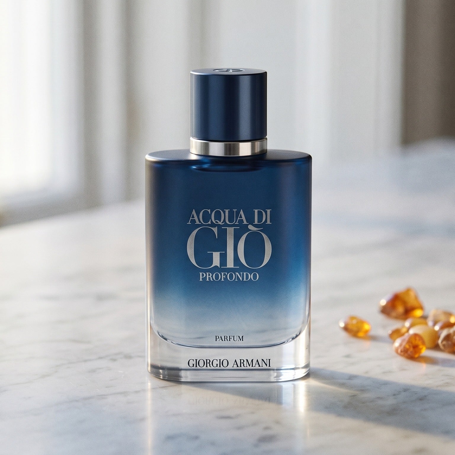 Acqua di Gio Profondo Parfum on pale grey marble with amber resin beads scattered to one side