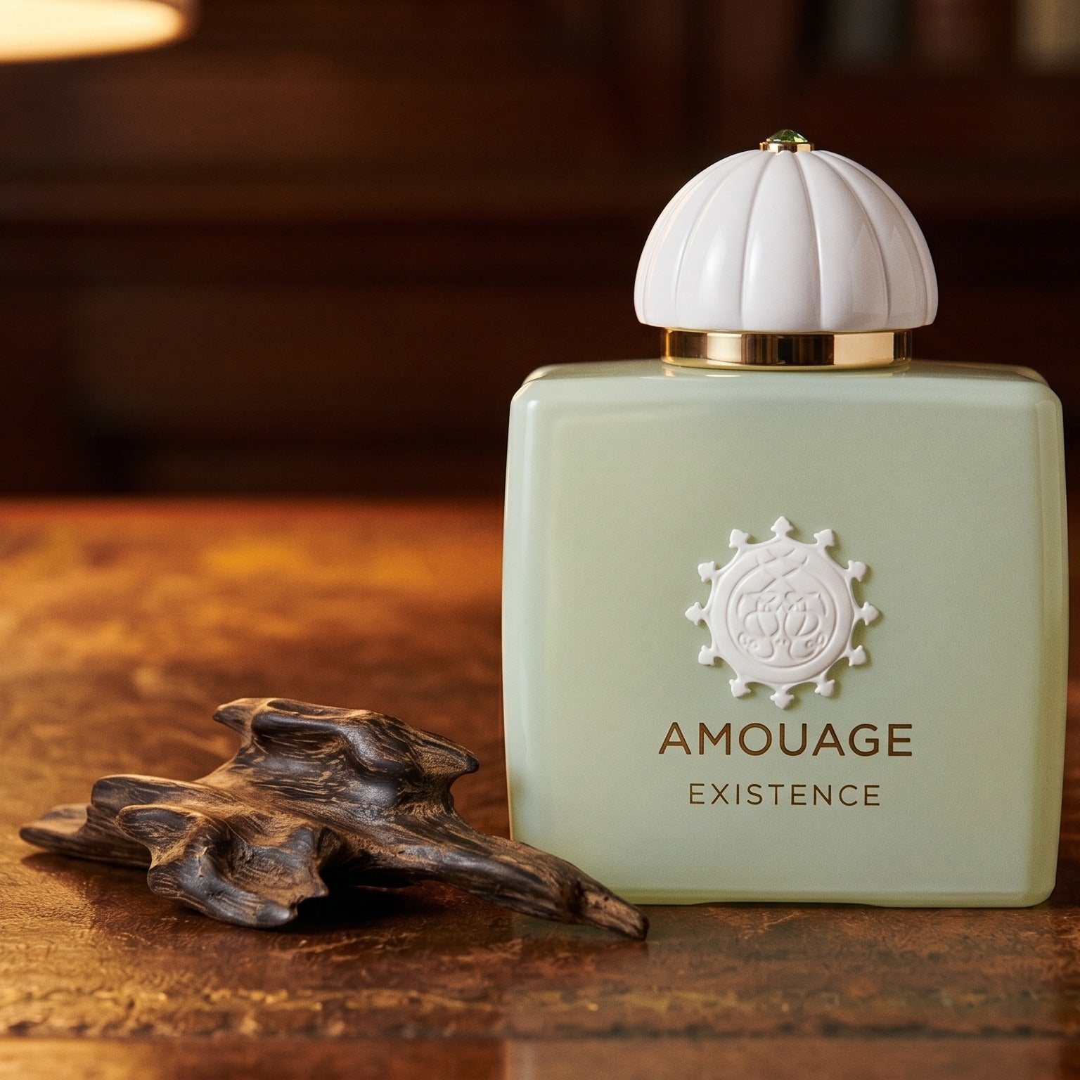 Amouage Existence EDP on aged leather-topped desk with a single agarwood chip beside the bottle
