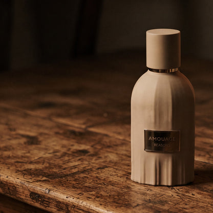 Amouage Reasons Essence de Parfum on aged teak with a candle burning gently to frame-right