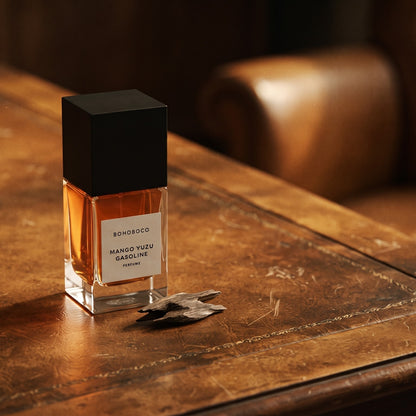 Bohoboco Mango Yuzu Gasoline Perfume on aged leather-topped desk with a single agarwood chip beside the bottle