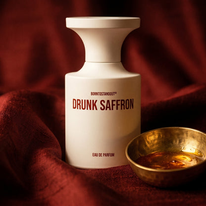 Borntostandout Drunk Saffron EDP on russet silk with a matte brass bowl holding tonka and amber pieces