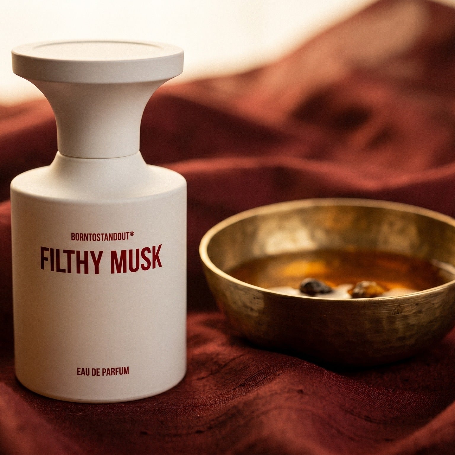 Borntostandout Filthy Musk EDP on cinnamon-tone silk with a shallow saucer of warm benzoin resin