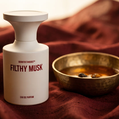 Borntostandout Filthy Musk EDP on cinnamon-tone silk with a shallow saucer of warm benzoin resin