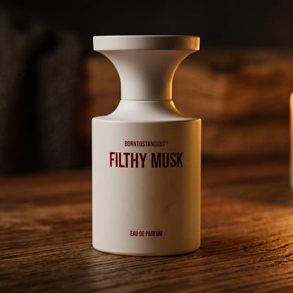 Borntostandout Filthy Musk EDP on aged maple with a slender candlestick and drifting smoke