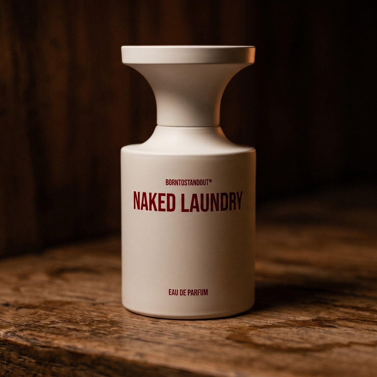 Borntostandout Naked Laundry EDP on aged teak with a candle burning gently to frame-right