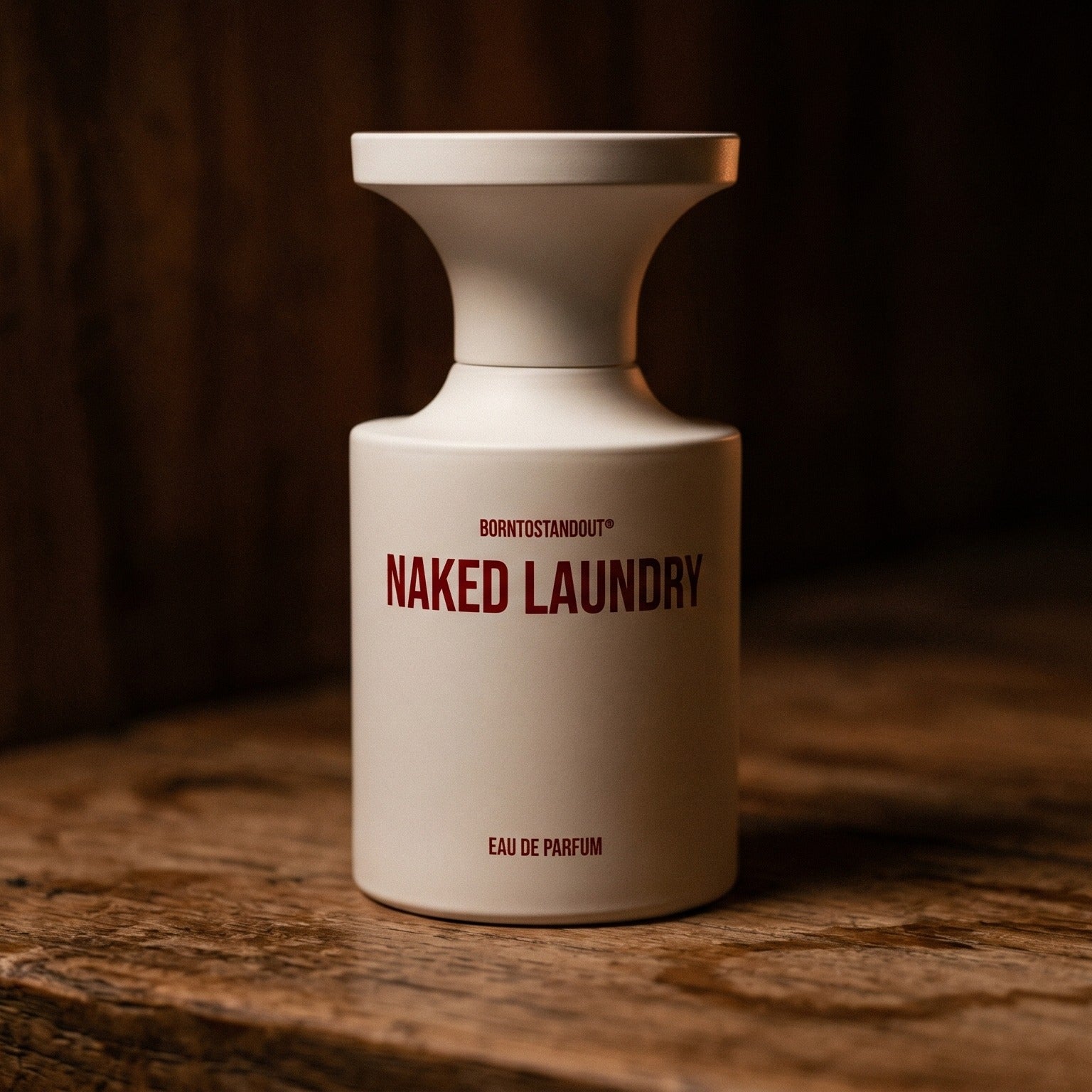 Borntostandout Naked Laundry EDP on aged teak with a candle burning gently to frame-right