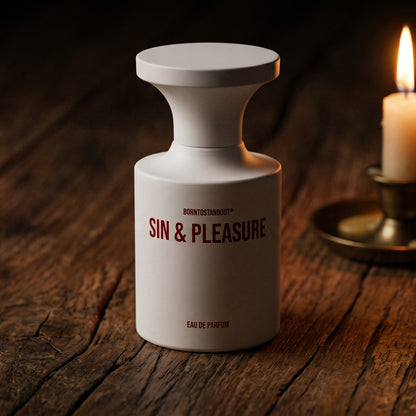 Borntostandout Sin & Pleasure EDP on aged teak with a candle burning gently to frame-right