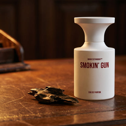 Borntostandout Smokin Gun EDP on dark tan leather desk with a brass lamp casting a warm pool of light