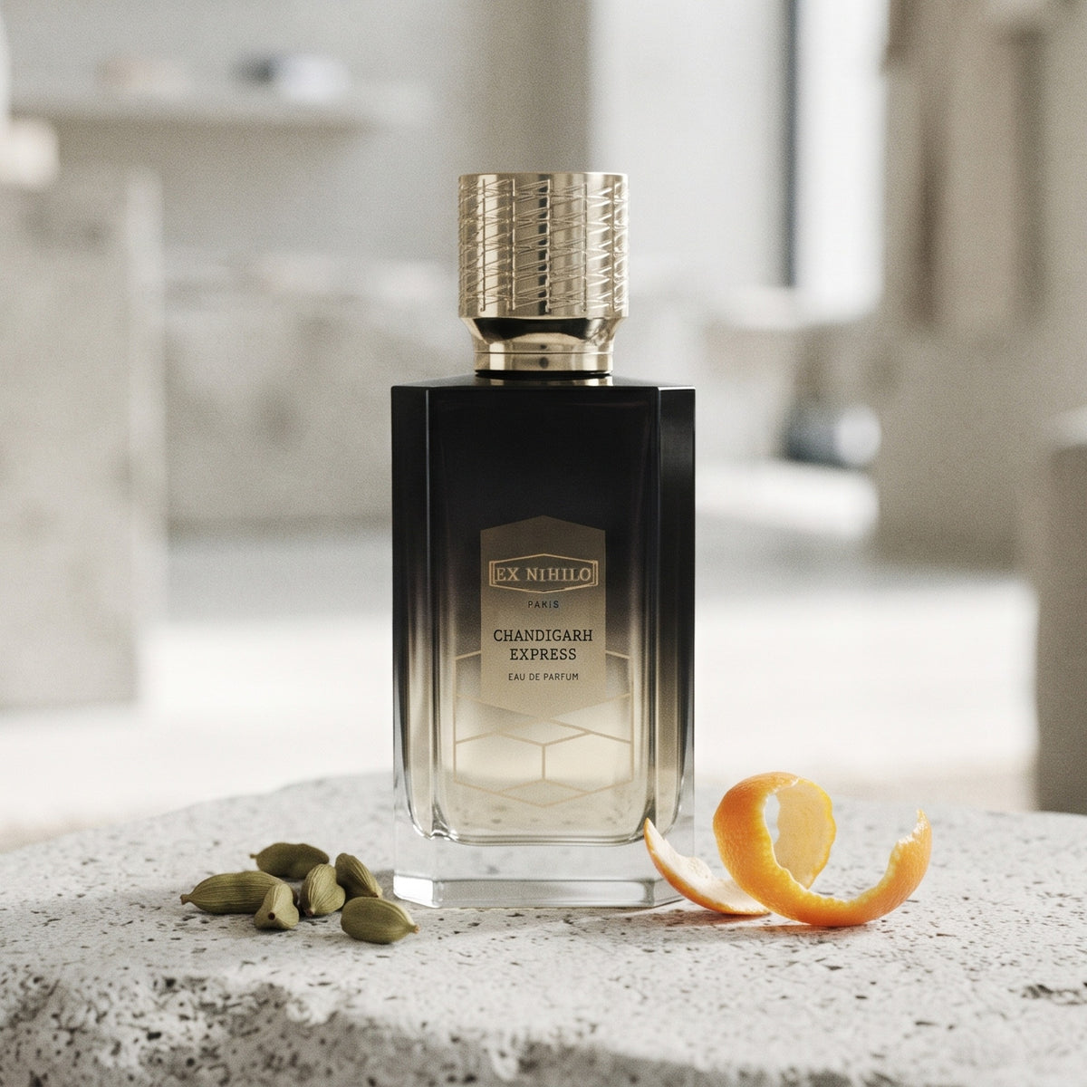 Ex Nihilo Chandigarh Express EDP on pale grey stone with green cardamom pods and a curl of mandarin peel