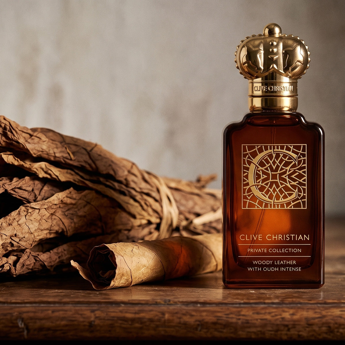 Clive Christian Private Collection C Woody Leather Oud on aged walnut console with a loose bundle of dried tobacco leaves