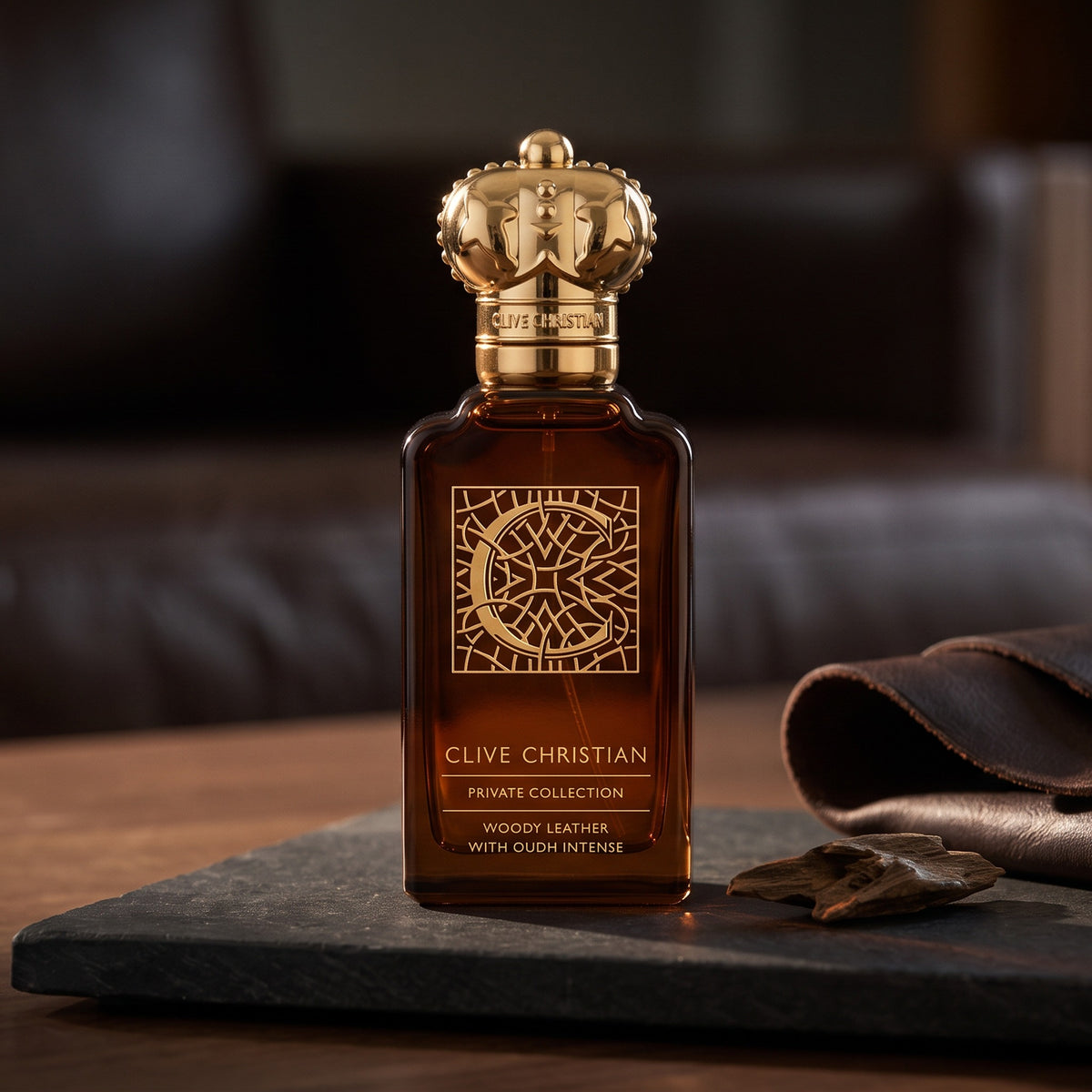 Clive Christian Private Collection C Woody Leather Oud on charcoal stone slab with a single agarwood chip beside a folded strip of dark leather