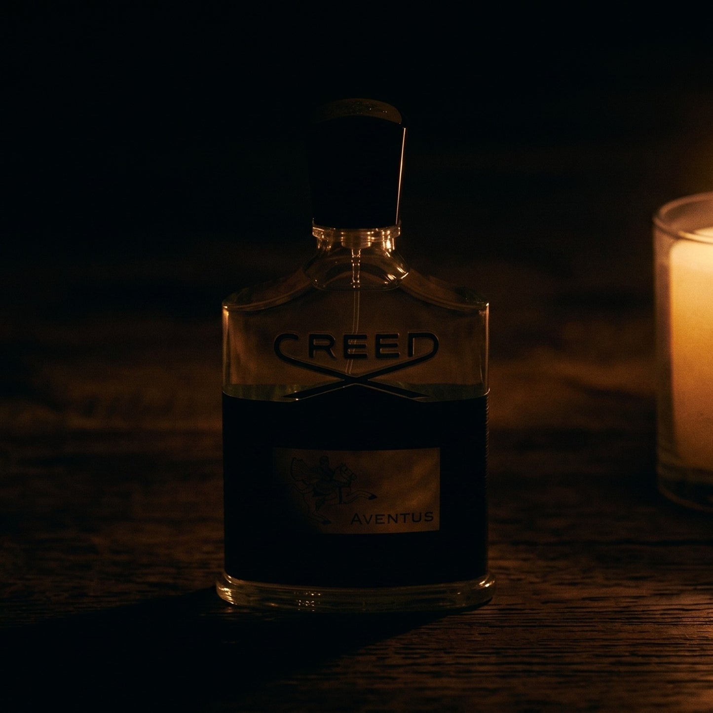 Creed Aventus on aged teak with a candle burning gently to frame-right