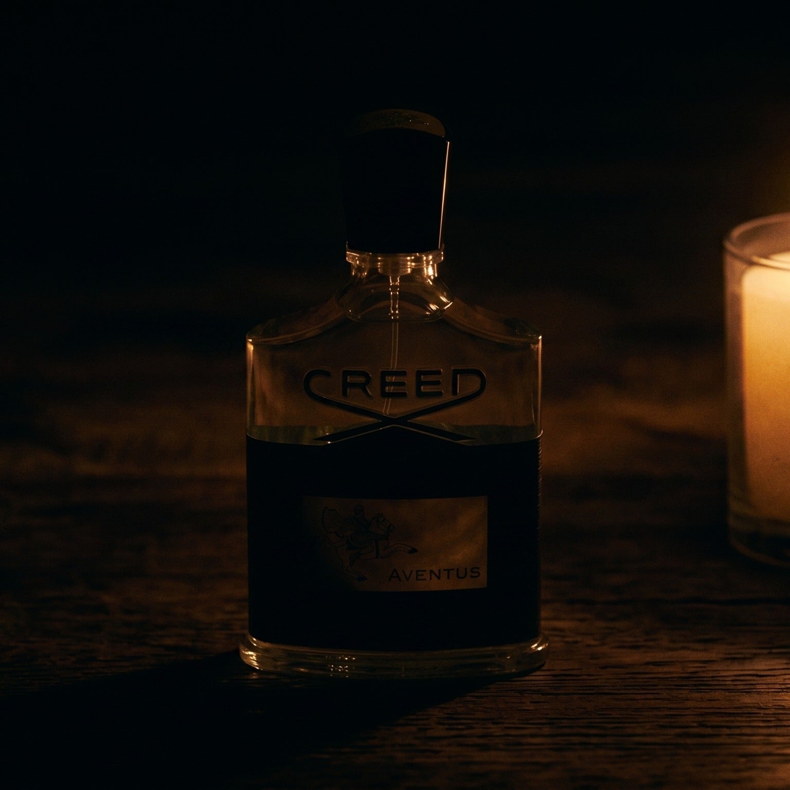 Creed Aventus on aged teak with a candle burning gently to frame-right