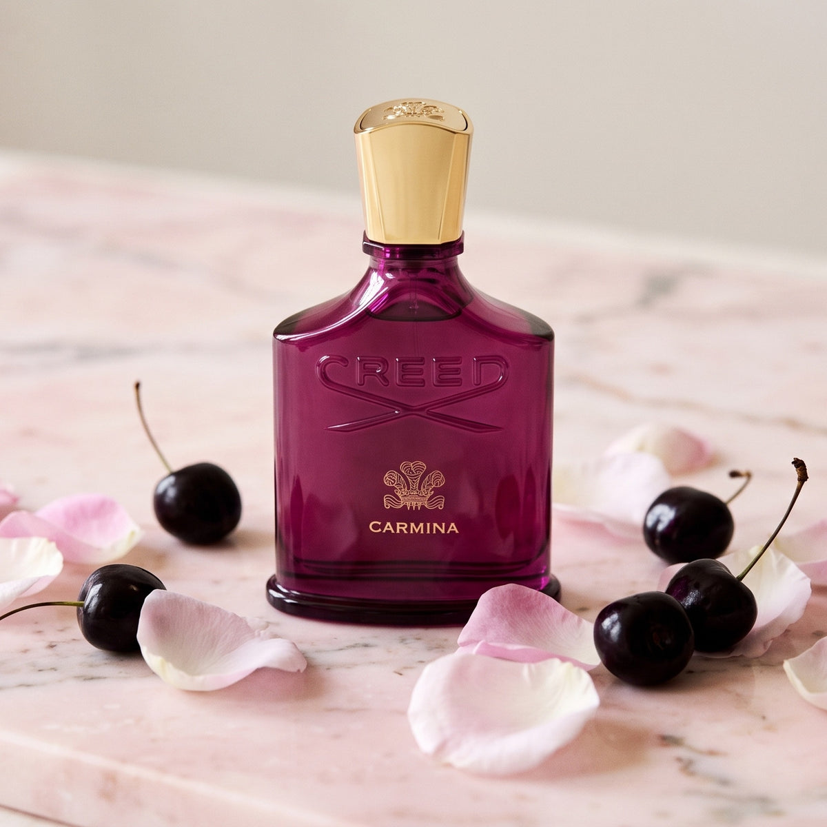 Creed Carmina on pale pink marble with Rose de Mai petals and a few black cherries