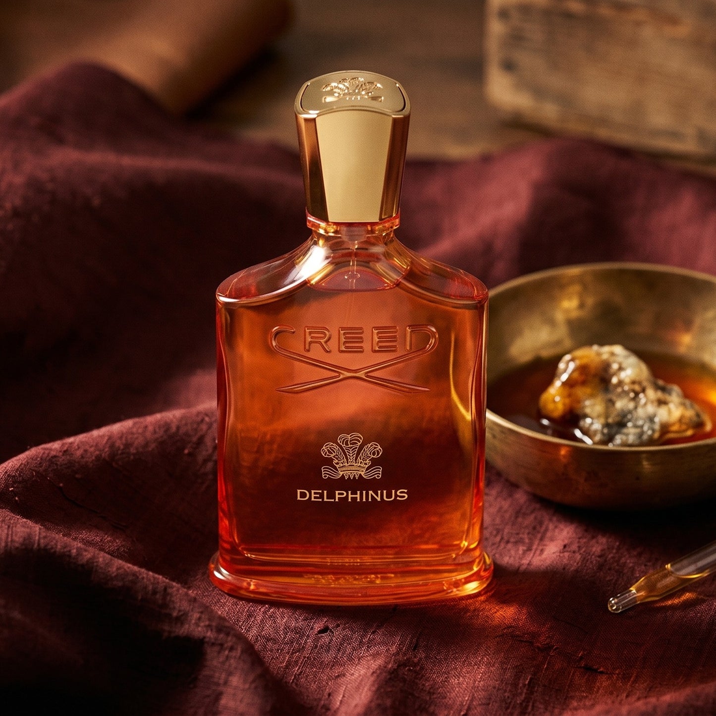 Creed Delphinus on russet silk with a matte brass bowl holding tonka and amber pieces