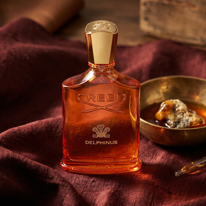 Creed Delphinus on russet silk with a matte brass bowl holding tonka and amber pieces